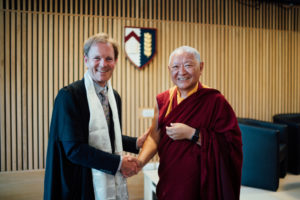 Ringu Tulku Rinpoche and Jonathan Michie, who is wearing a traditional Tibetan ceremonial scarf, stood shaking hands in front of the Kellogg crest