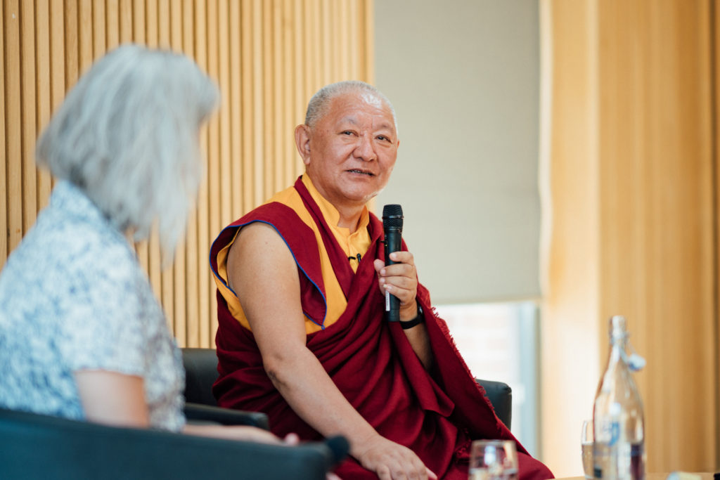 Ringu Tulku Rinpoche seated on the stage speaking to Mary Henenghan