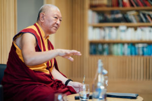 Close up shot from the side of Ringu Tulku Rinpoche seated on the stage addressing the audience