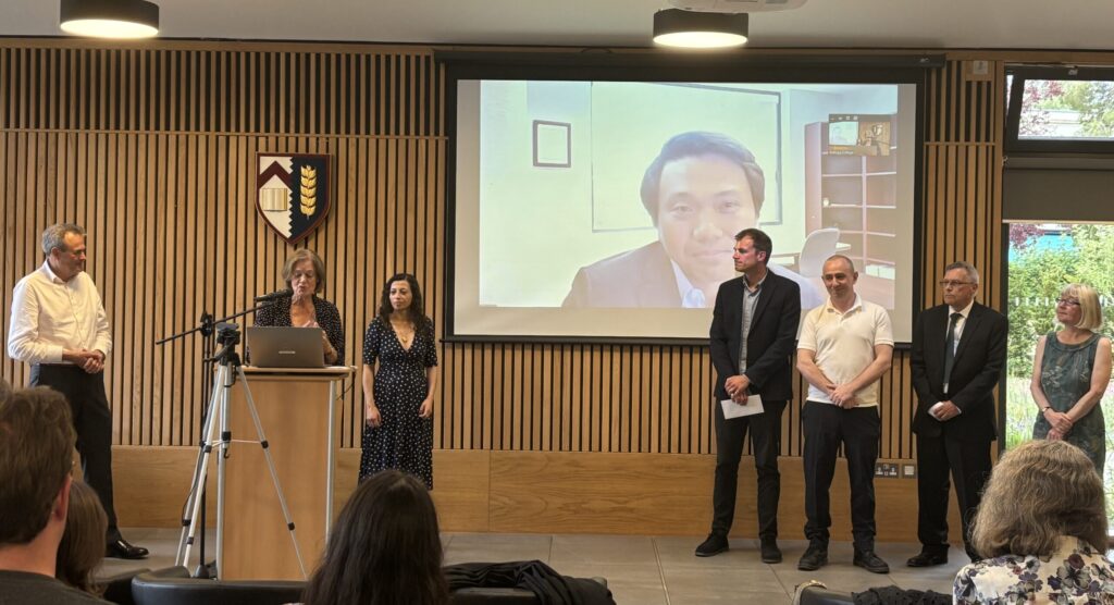 Dr Clare Morgan presenting the awards in to a crowd with judges stood on the right hand side.