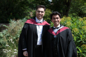 Two students in graduation gowns smiling.