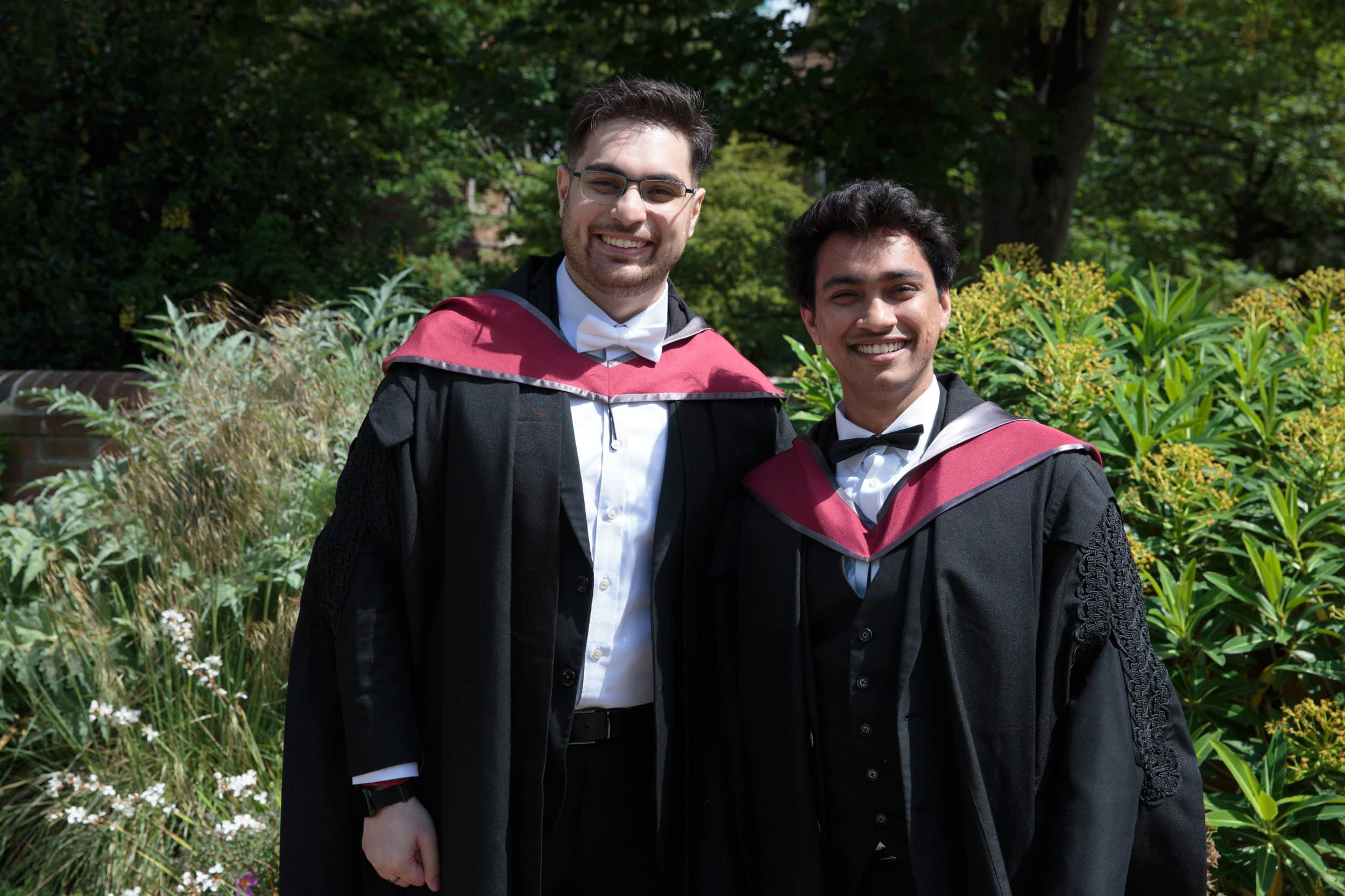 Two students in graduation gowns smiling.