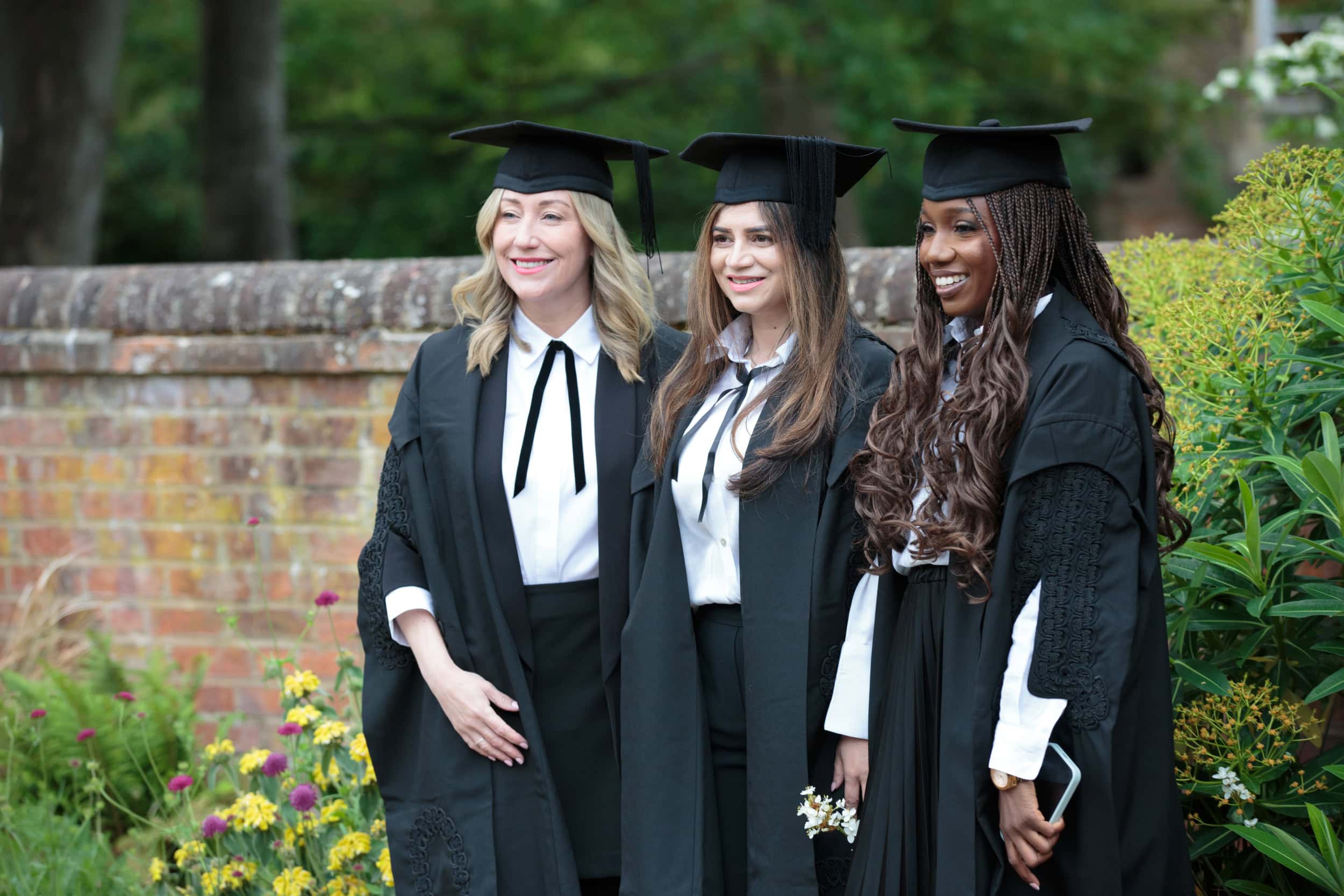 Group of three graduates stood together smiling at the camera
