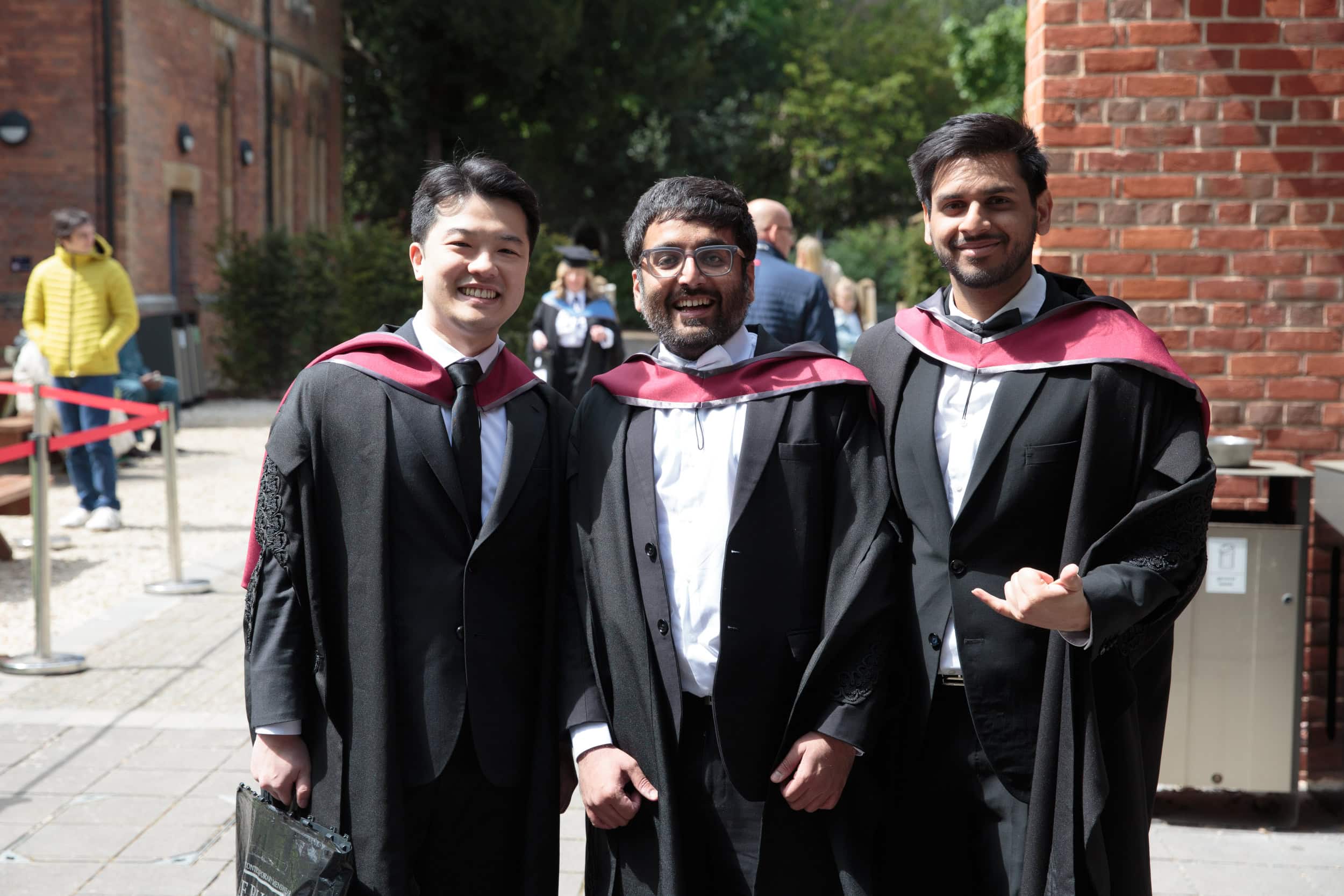 Three students in graduation gowns stood outside the Hub smiling.