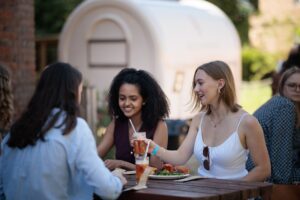 Guests enjoying lunch together at picnic benches beneath parasols.
