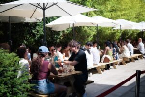 Guests seated together at picnic benches in the sunshine.