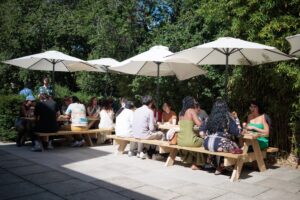 Guests seated together at picnic benches in the sunshine.