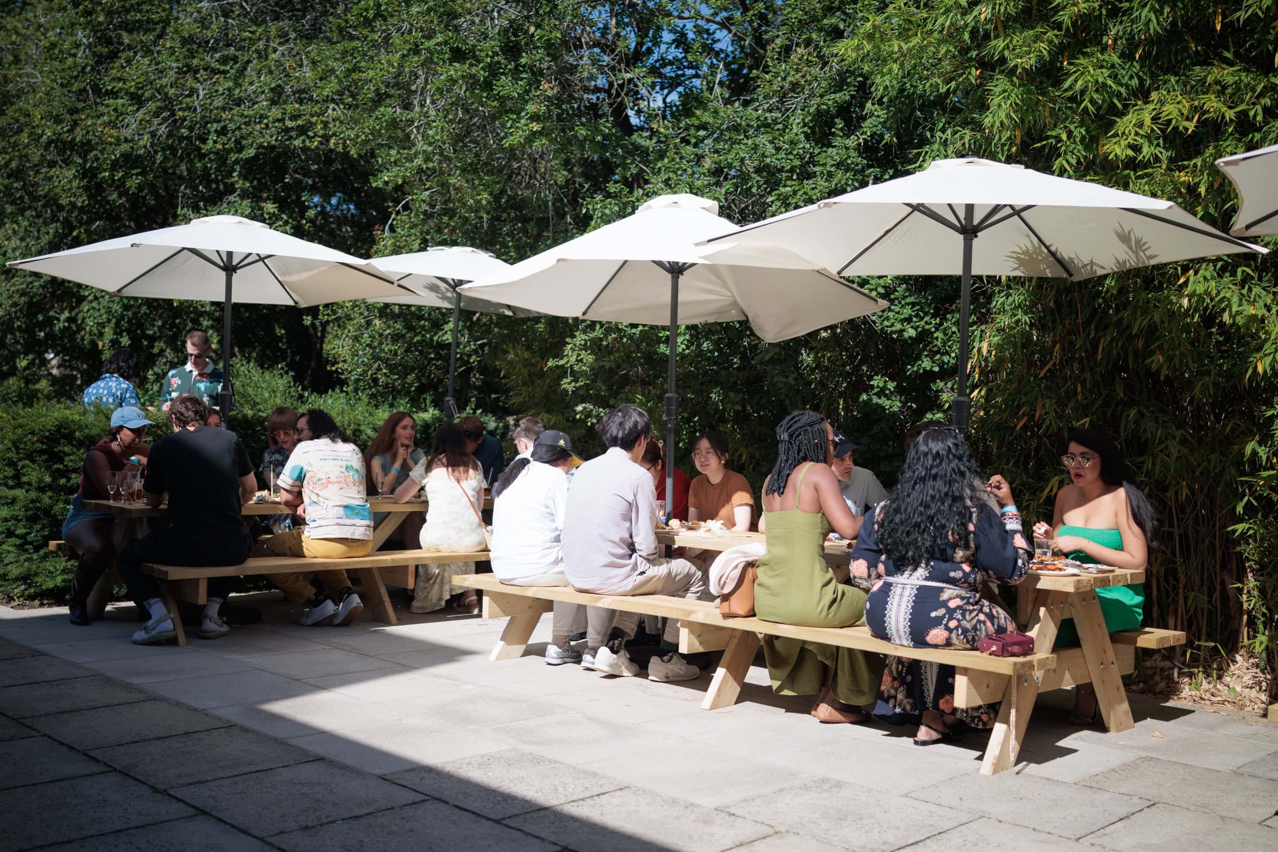 Guests seated together at picnic benches in the sunshine.